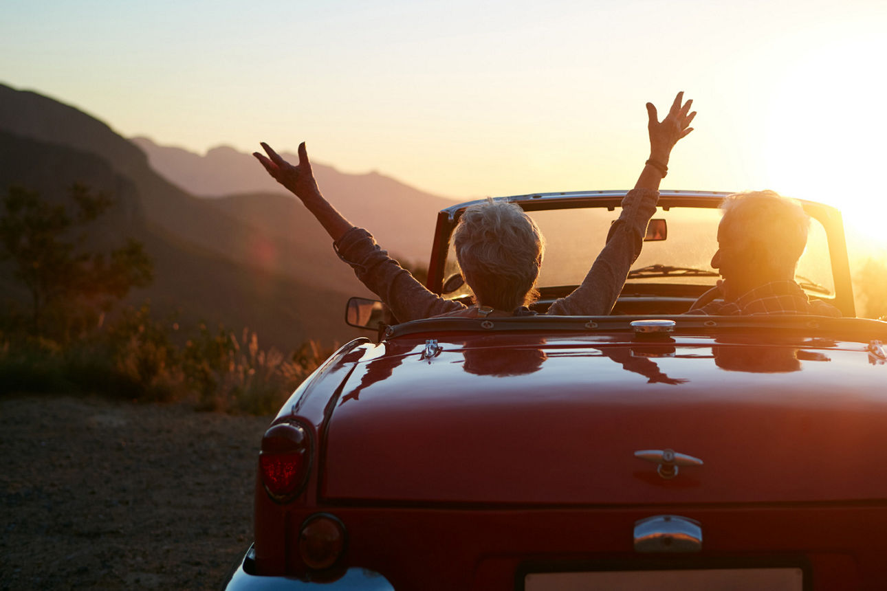 Ein Paar sitzt in einem Cabrio und schaut sich den Sonnenuntergang an. 