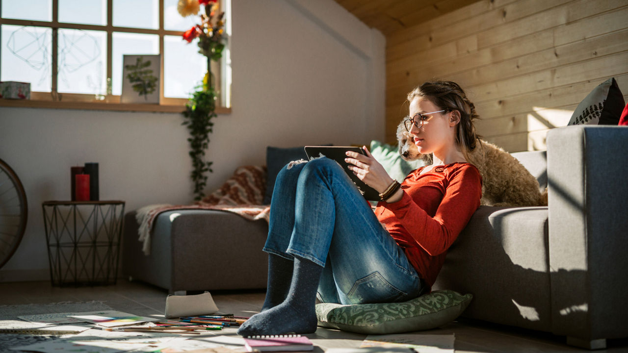 Eine Frau sitzt auf dem Boden mit Tablet in der Hand und blickt hinein.
