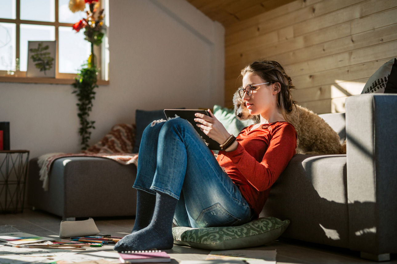 Eine Frau sitzt auf dem Boden mit Tablet in der Hand und blickt hinein.