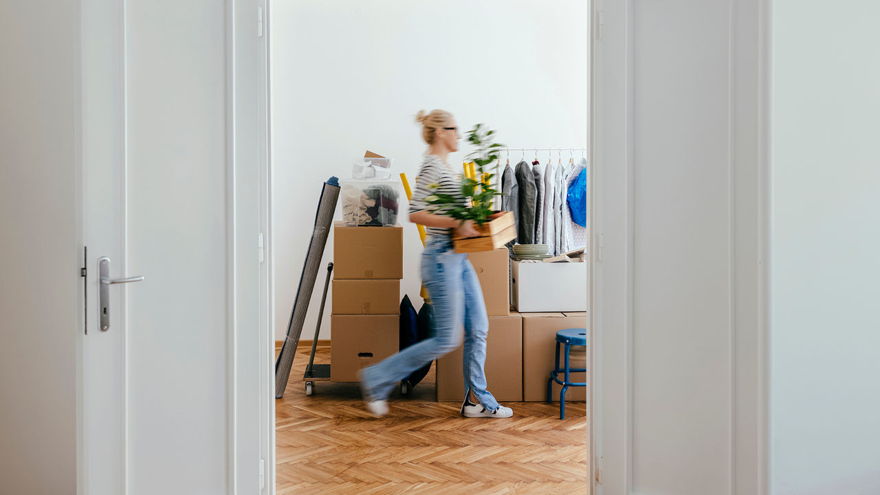 Eine Frau mit Kartons und Umzugsgegenständen in einer hellen Wohnung. 