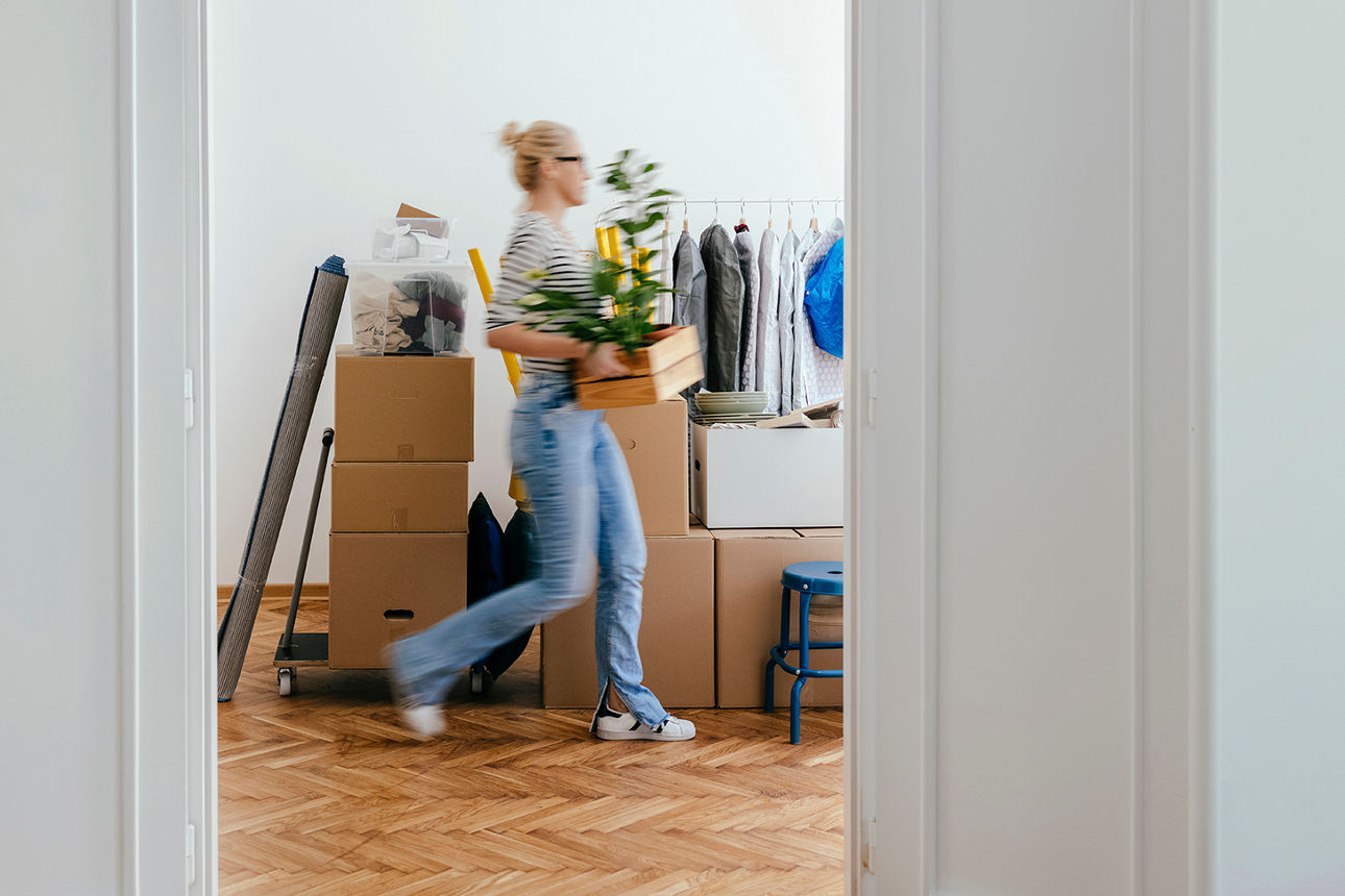 Eine Frau mit Kartons und Umzugsgegenständen in einer hellen Wohnung. 