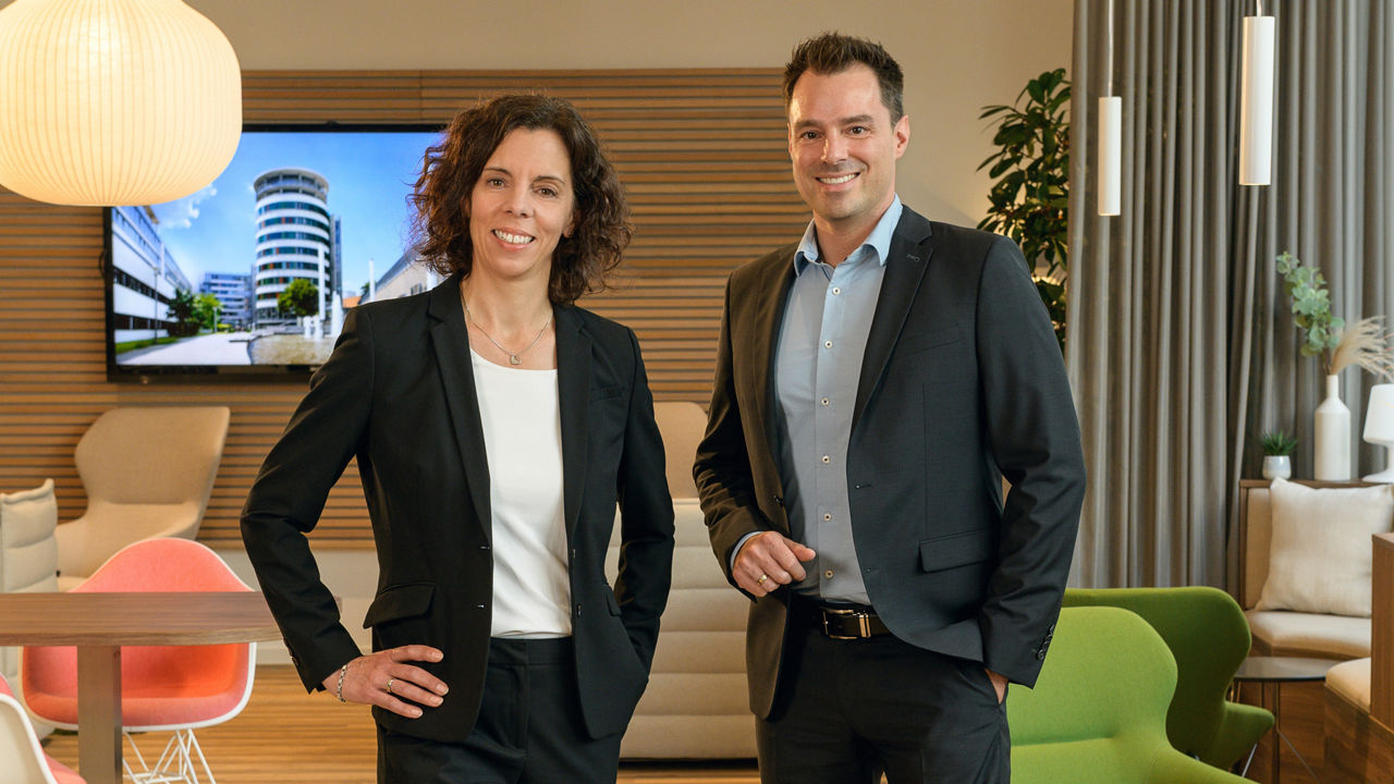 Frau Sonja Kelkel und Herr Christian Berle aus dem Vorstand lächeln in die Kamera. Sie stehen nebeneinander.