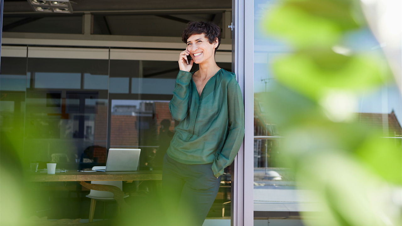 Eine Frau lehnt an der Terrassentür und telefoniert