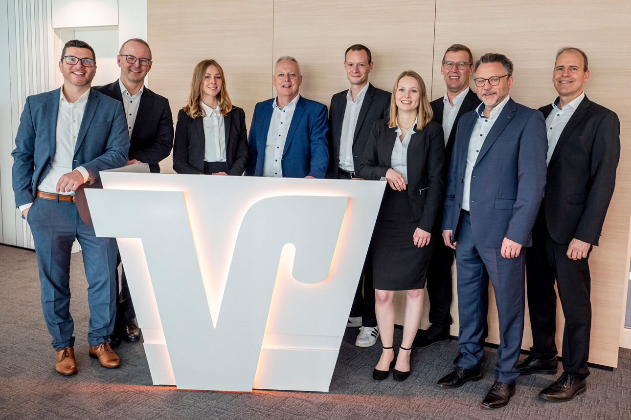 Sieben Männer und zwei Frauen stehen beieinander