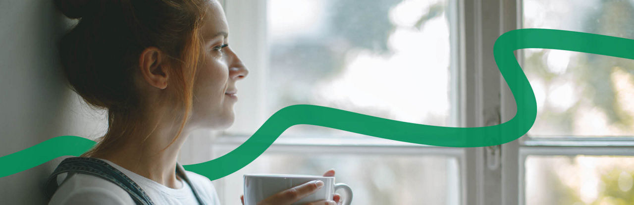 Eine Frau hält eine Tasse in den Händen und schaut aus dem Fenster