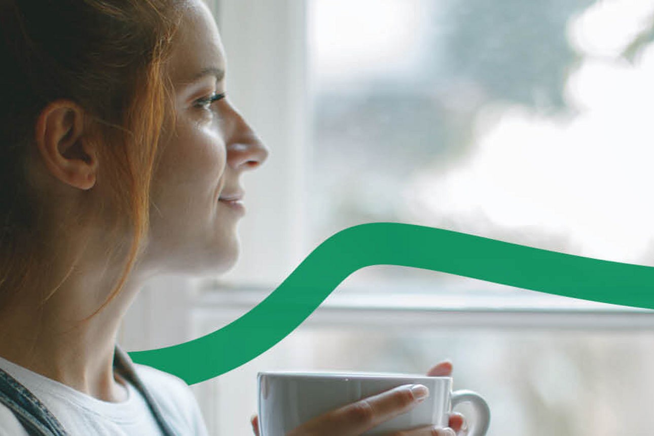 Eine Frau hält eine Tasse in den Händen und schaut aus dem Fenster