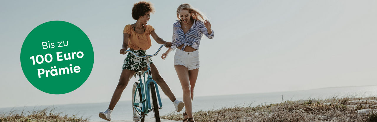 Eine junge Frau auf einem Fahrrad und eine junge Frau zu Fuß gehen am Strand spazieren