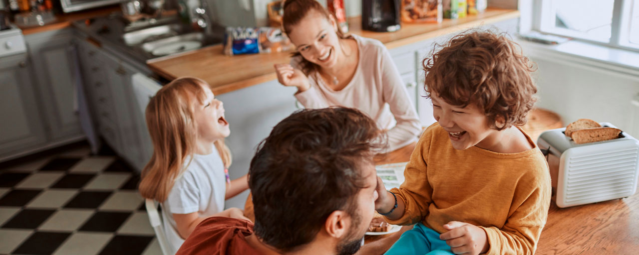 Mutter, Vater und zwei Kinder lachen zusammen am Frühstückstisch