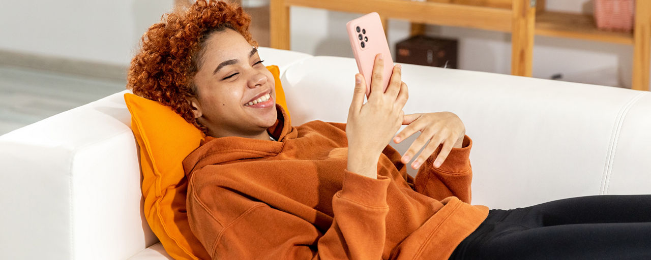 Junge Person liegt mit Handy auf einem Sofa