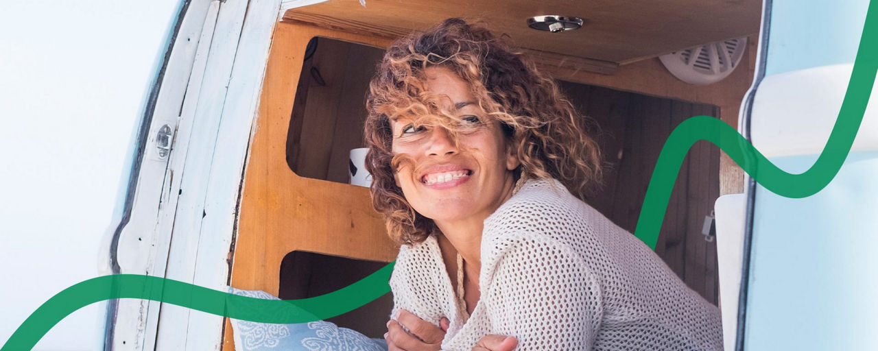 Eine Frau schaut aus einem Campervan, im Hintergrund ist das Meer zu sehen