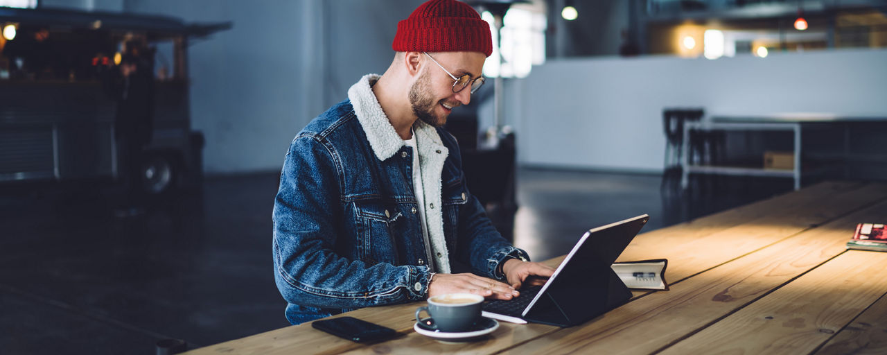 Person mit Laptop und Kaffee an langem Holztisch sitzend