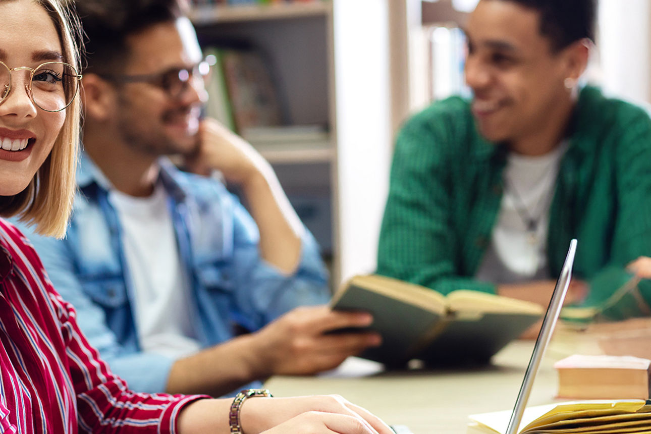 Studentin schaut lächelnd nach vorne, zwei Studenten im Hintergrund unterhalten sich