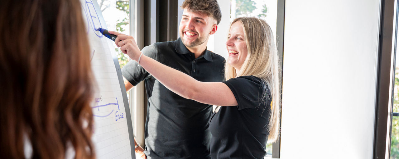 Junge Frau zeigt einem jungen Mann am Flipchart etwas