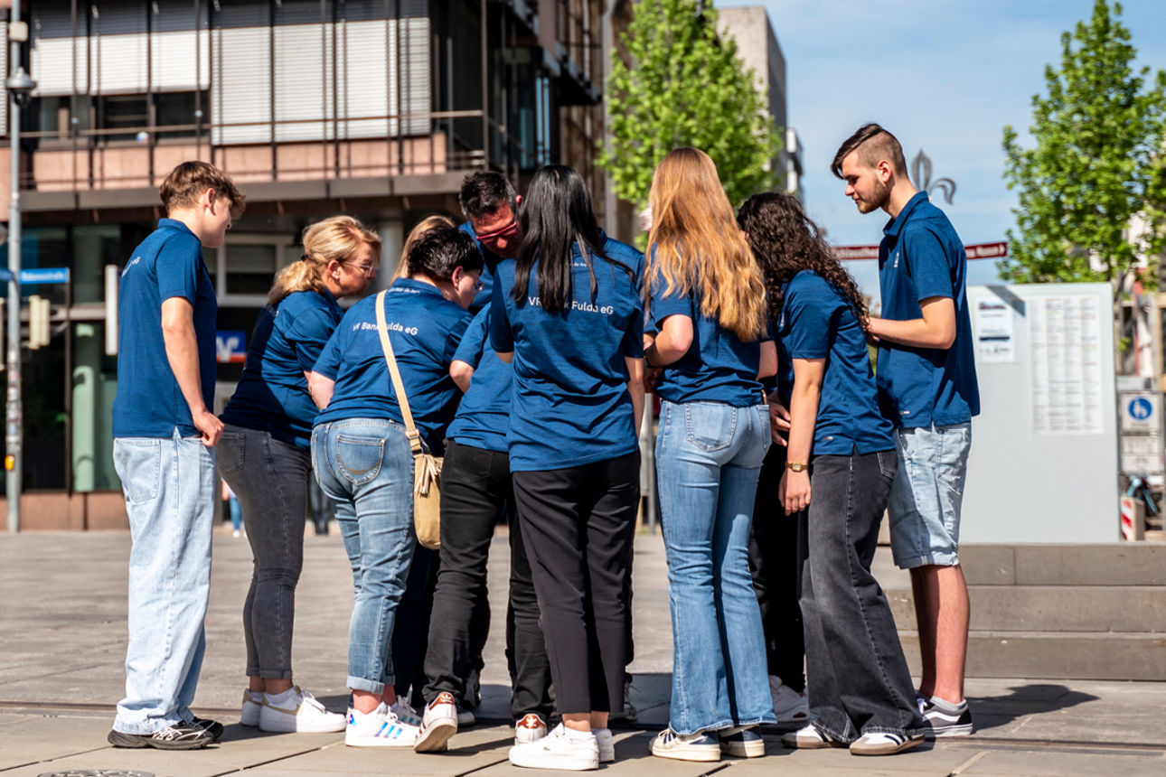Zu sehen ist eine Gruppe von Auszubildende auf dem Uniplatz in Fulda. Im Hintergrund ist die Bankfiliale in der Bahnhofstraße