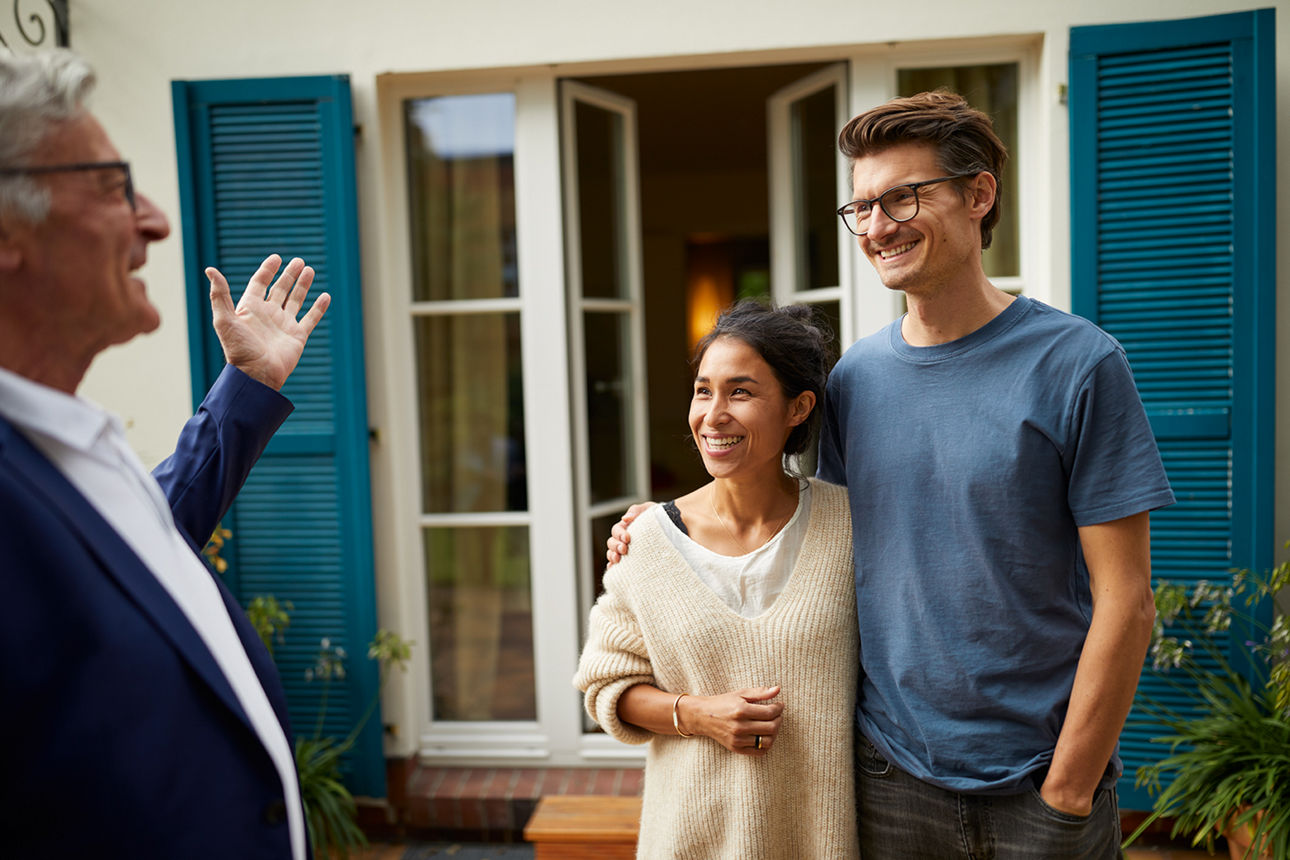 Ein Prächen steht vor einem HAus mit offenen Fenstern. Vor ihnen steht ein Mann, der einen Berater darstellen soll.