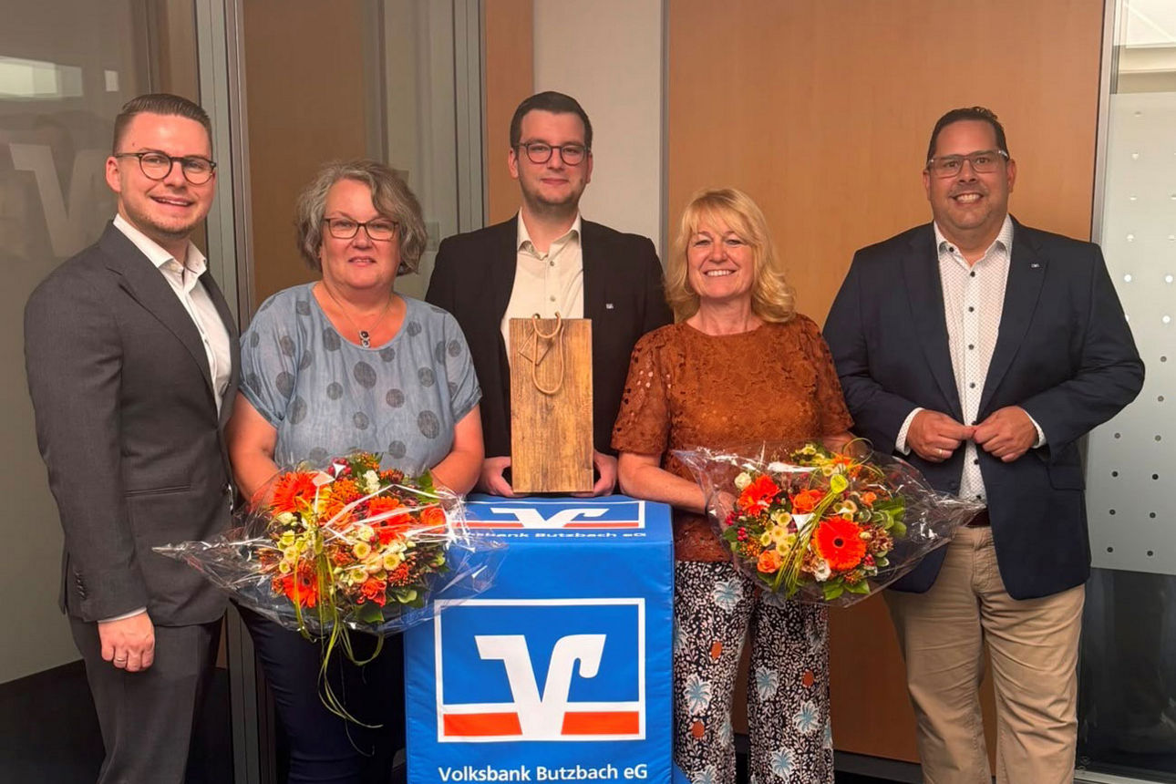 Zwei Mitarbeiterinnen der Volksbank Butzbach eG mit Blumensträußen zwischen drei Männern in Anzügen