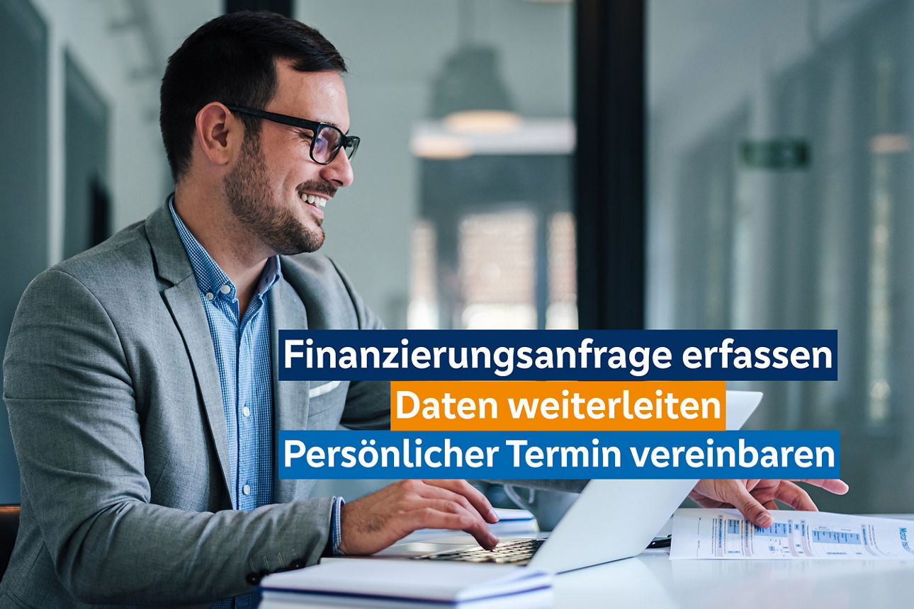 Ein Mann sitzt an einem Tisch in einer modernen Büro. Vor ihm ist sein Notebook aufgeklappt.