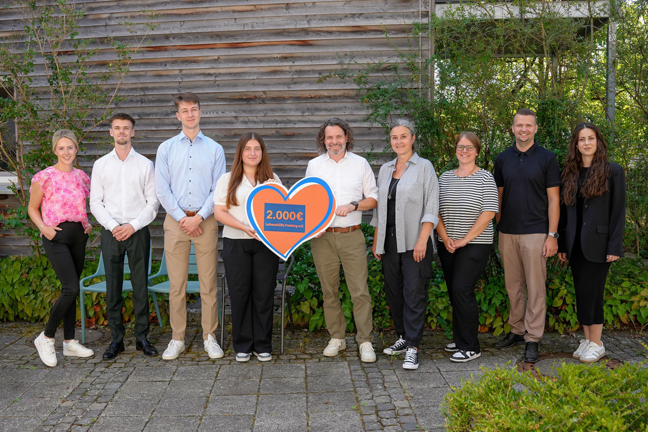 Gruppenbild mit neun Personen, zwei in der Mitte halten ein orangenes Spendenherz über 2.000 Euro