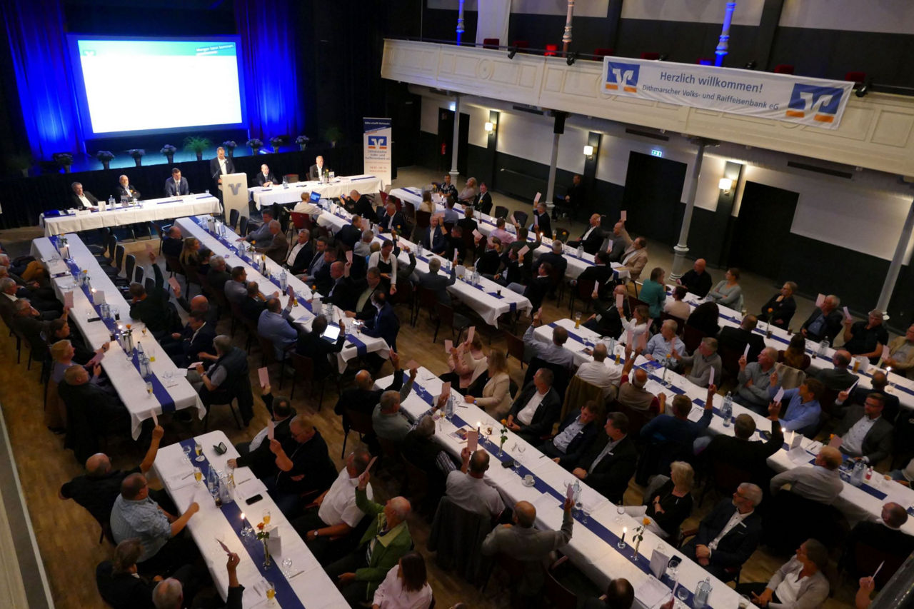 Menschen sitzen an Tischen und halten Abstimmungskarten hoch