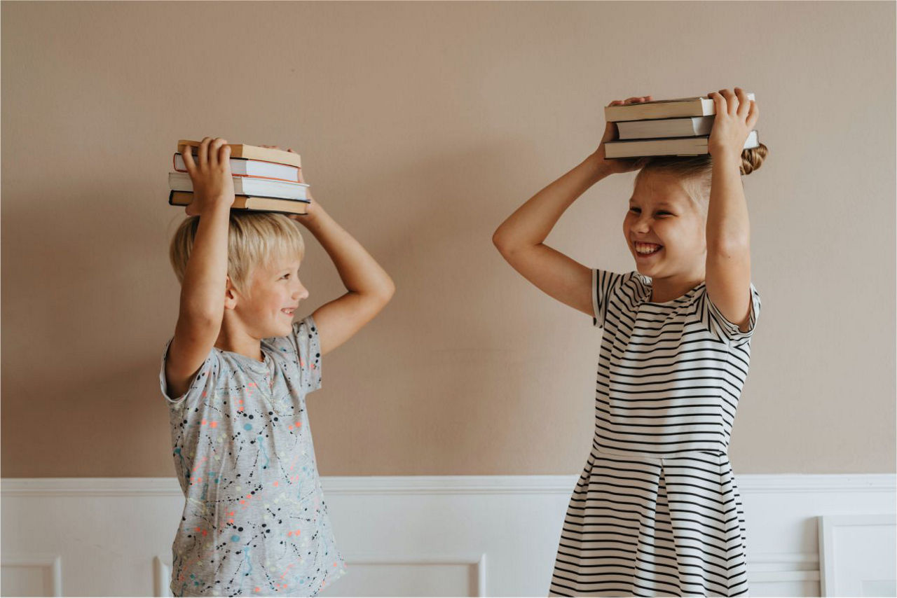 Zwei Kinder lachen und halten Bücher auf dem Kopf fest