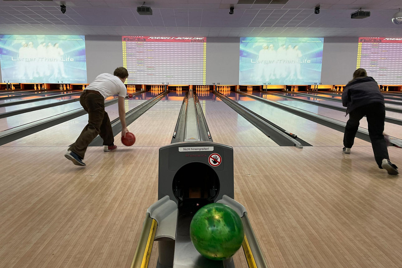 Zwei Personen die je eine Bowlingkugel werfen