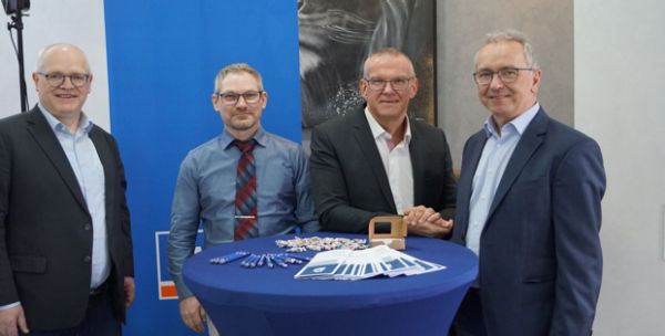 Vier Männer in Business-Kleidung stehen vor einem blauen Transparent.