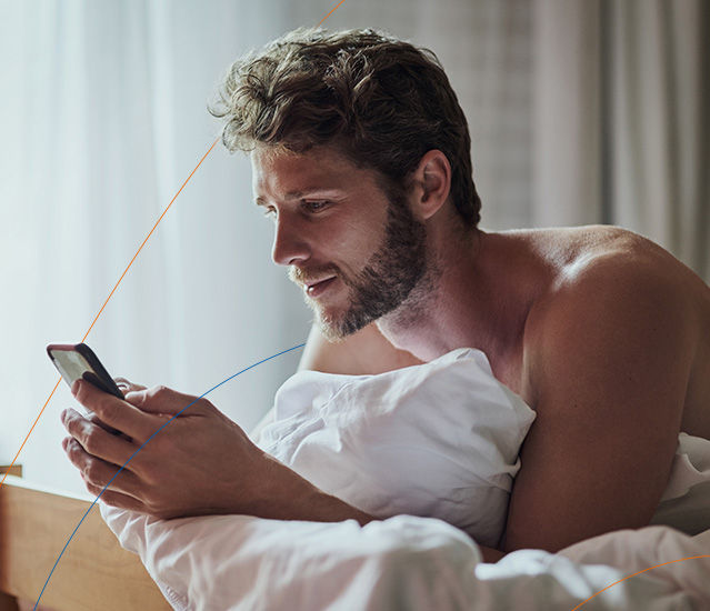 Mann liegt mit Smartphone auf Bett und nutzt den Kontowechselservice um einfach seine Bank zu wechseln