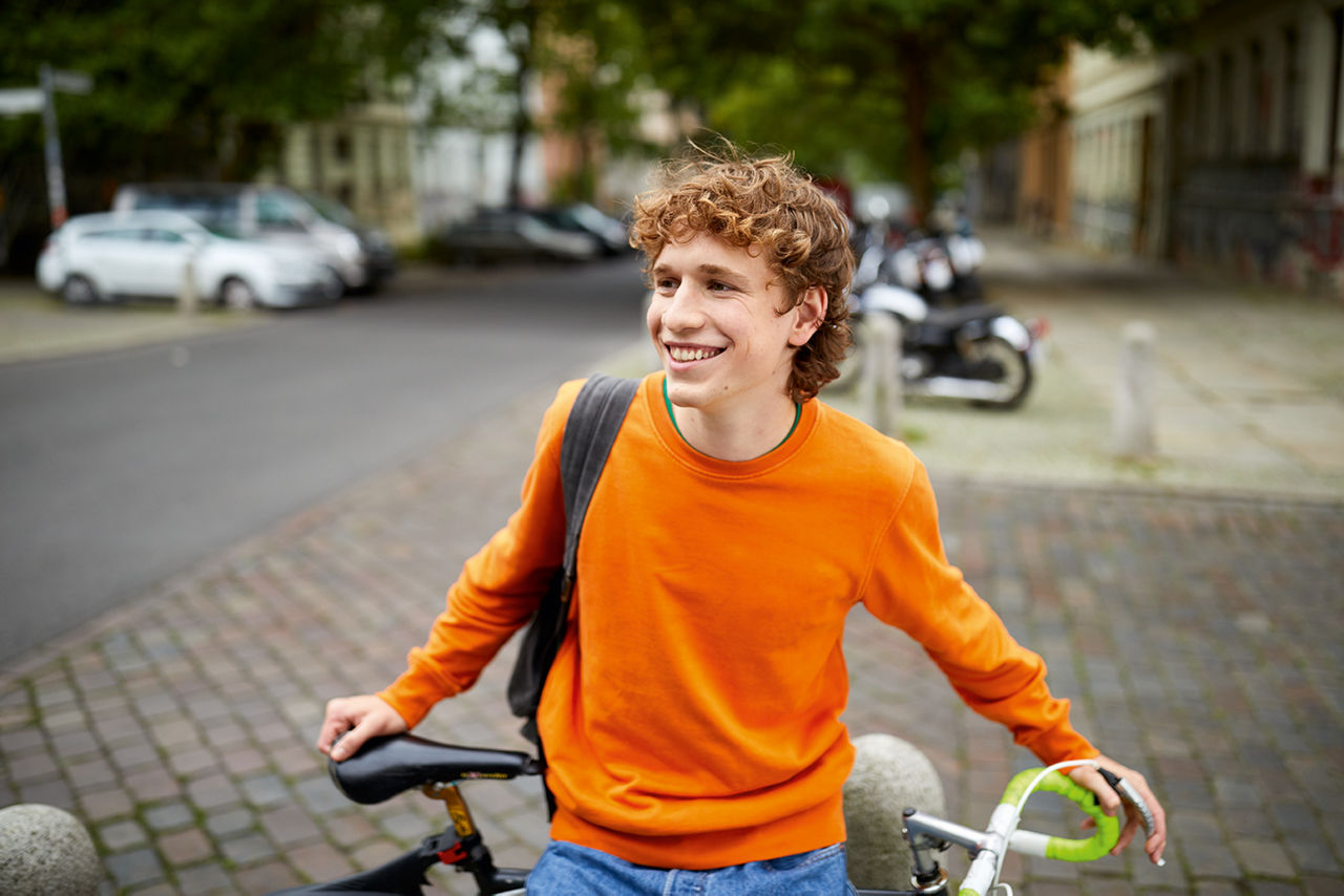 Jugendlicher lehnt an seinem Fahrrad mit einer Wohnstraße im Hintergrund