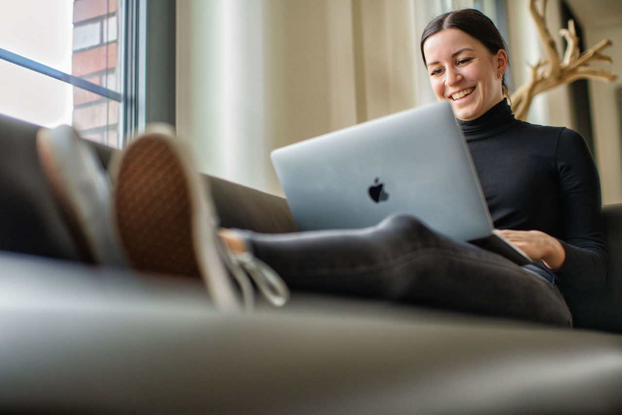 Junge Frau sitzt entspannt auf dem Sofa und hat einen Laptop auf dem Schoß