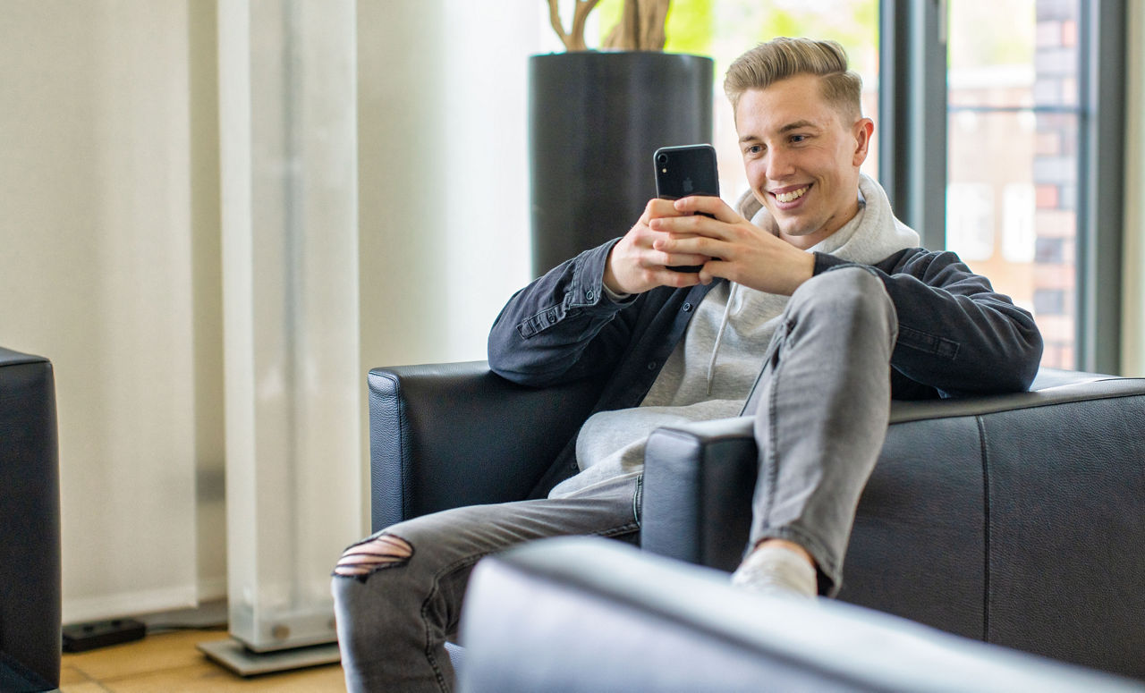 Ein Mann sitzt bequem auf einem Sessel und blickt auf sein Smartphone.