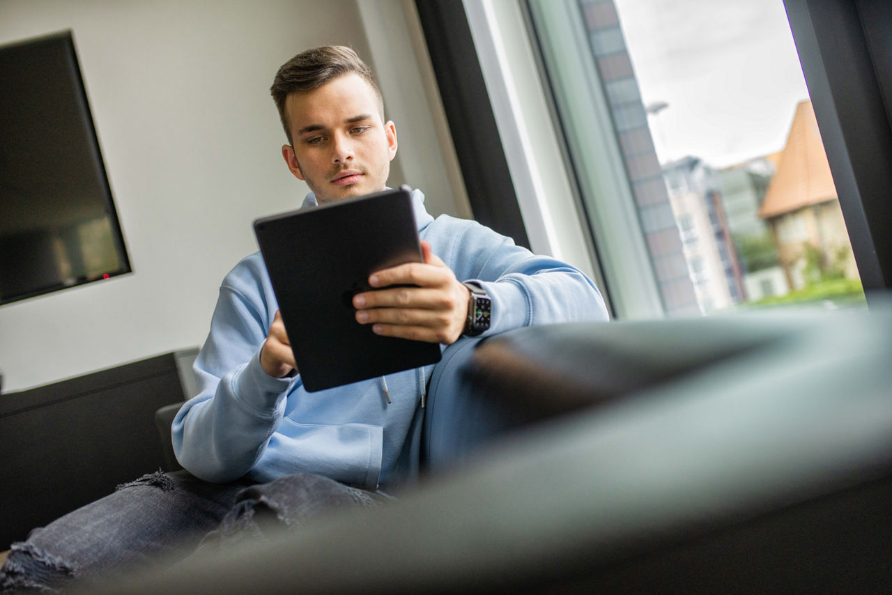 Junger Mann sitzt entspannt auf dem Sofa und schaut in sein Tablet