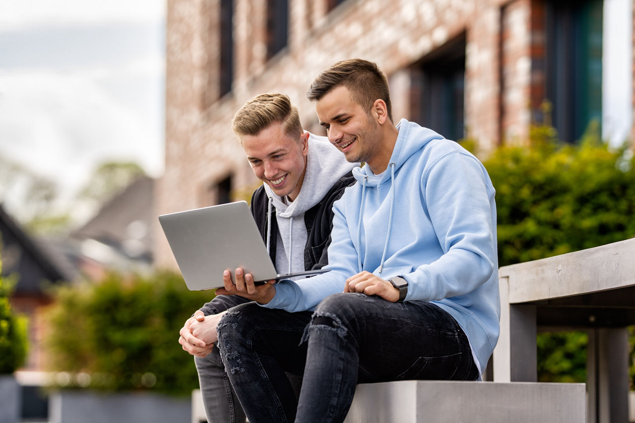 Zwei Männer sitzen nebeneinander mit einem Laptop in der Hand