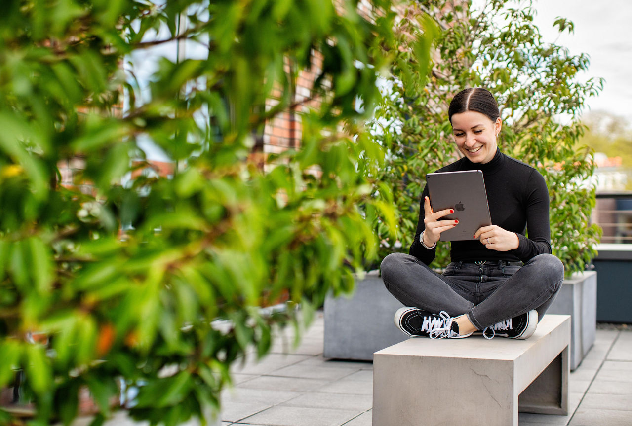 Junge Frau sitzt mit einem Tablet in der Hand auf einer Bank