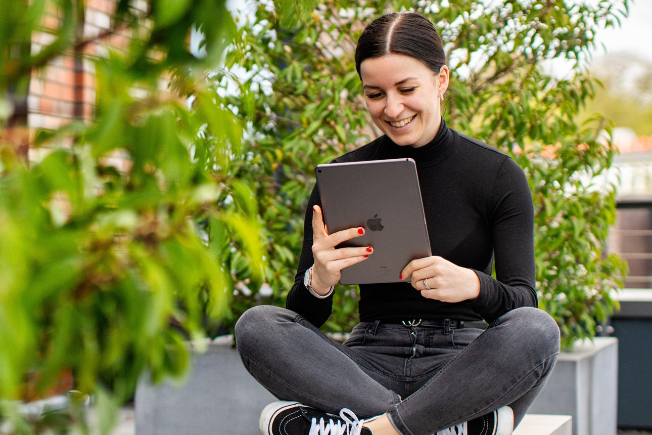 Junge Frau sitzt mit einem Tablet in der Hand auf einer Bank