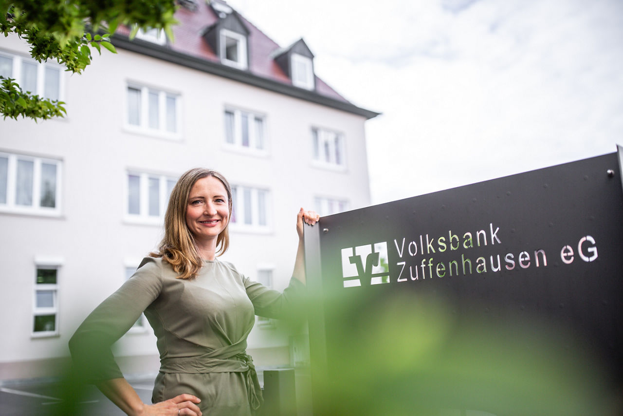 Eine Frau vor einem Bankgebäude an einem Volksbank Zuffenhausen eG Schild.