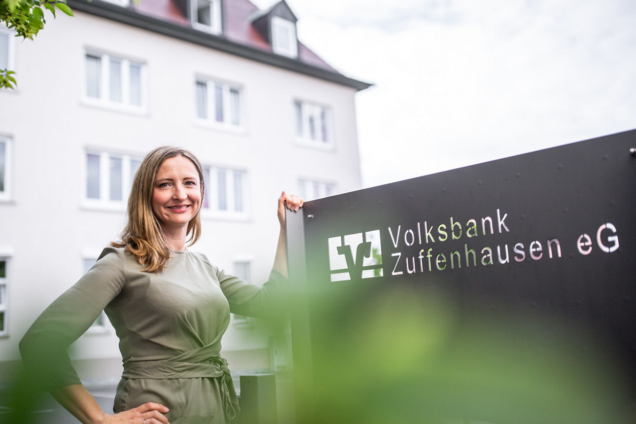 Eine Frau vor einem Bankgebäude an einem Volksbank Zuffenhausen eG Schild.