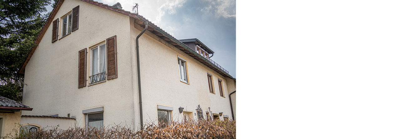 Ein altes sanierungsbedürftiges Haus von der Seite mit beigem Anstrich.