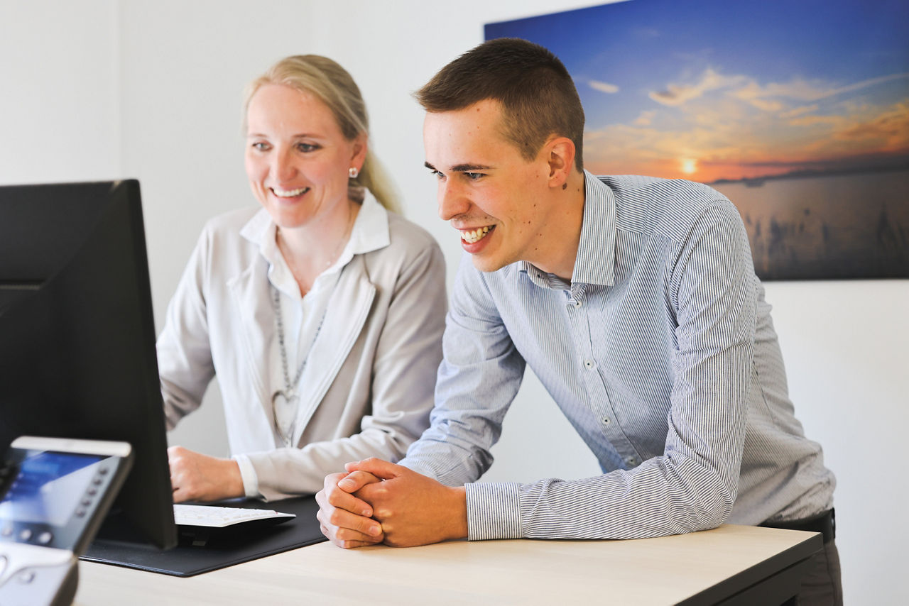 Eine Frau und ein Mann stehen an einem Schreibtisch vor einem Laptop