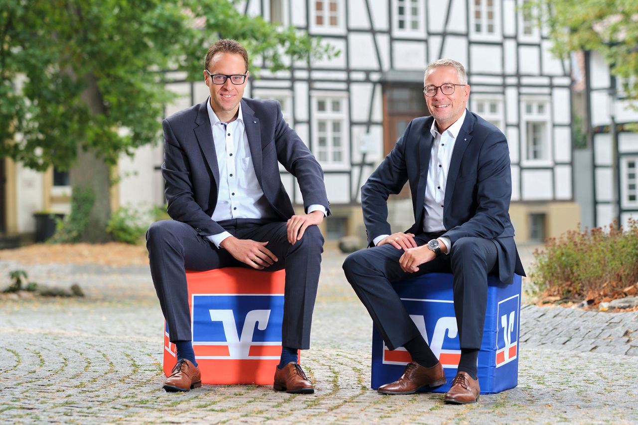 Die beiden Vorstandsmitglieder sitzen auf Sitzwürfel mit Volksbank-Symbol
