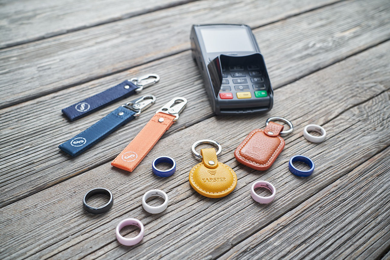 Auf einem Tisch liegen ein Kartenterminal und verschiedene Wearables wie Ringe und Schlüsselanhänger