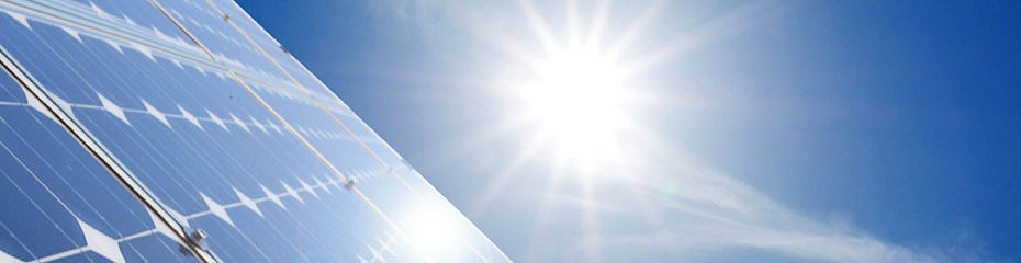 Die Sonne strahlt auf eine Photovoltaikanlage, die im linken Bereich des Bildes zu sehen ist. Der Himmel ist blau ohne Wolken..
