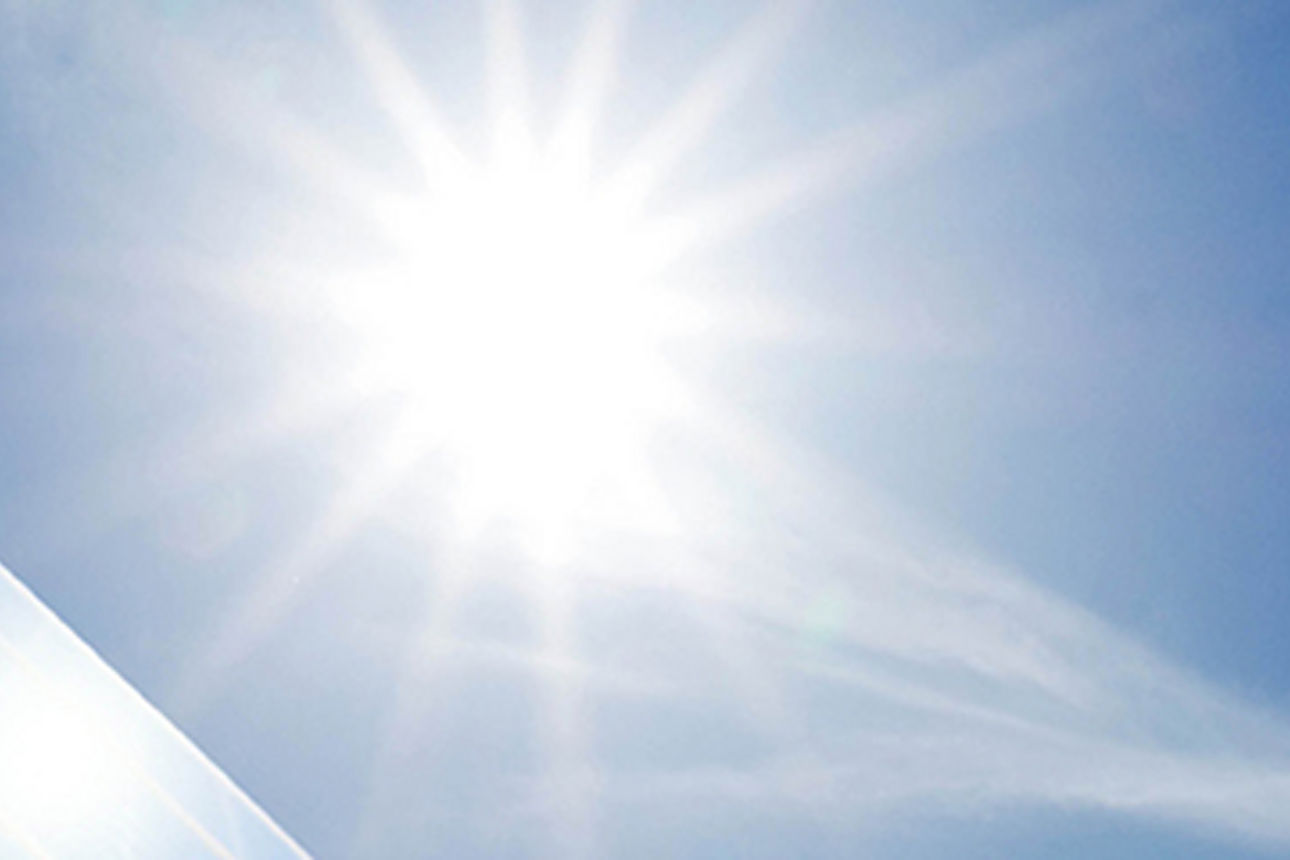 Die Sonne strahlt auf eine Photovoltaikanlage, die im linken Bereich des Bildes zu sehen ist. Der Himmel ist blau ohne Wolken..