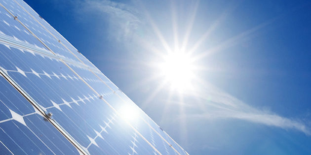 Die Sonne strahlt auf eine Photovoltaikanlage, die im linken Bereich des Bildes zu sehen ist. Der Himmel ist blau ohne Wolken..