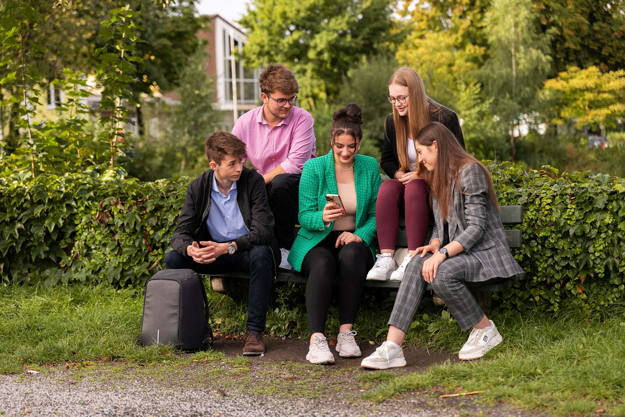 Azubis auf einer Bank mit Handy in der Hand