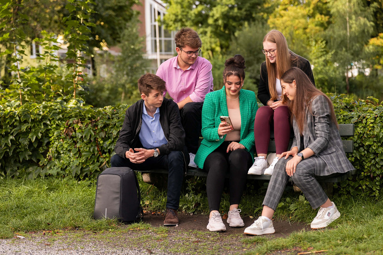 Azubis auf einer Bank mit Handy in der Hand