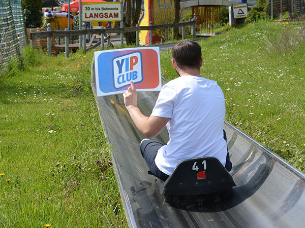 Ein junger Mann sitzt in einem Schlitten auf einer Metallrutsche