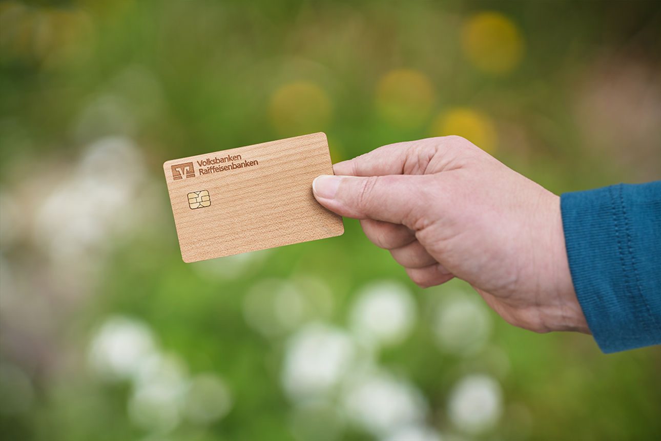 Eine Hand hält eine Holzkarte vor einem grünen Hintergrund