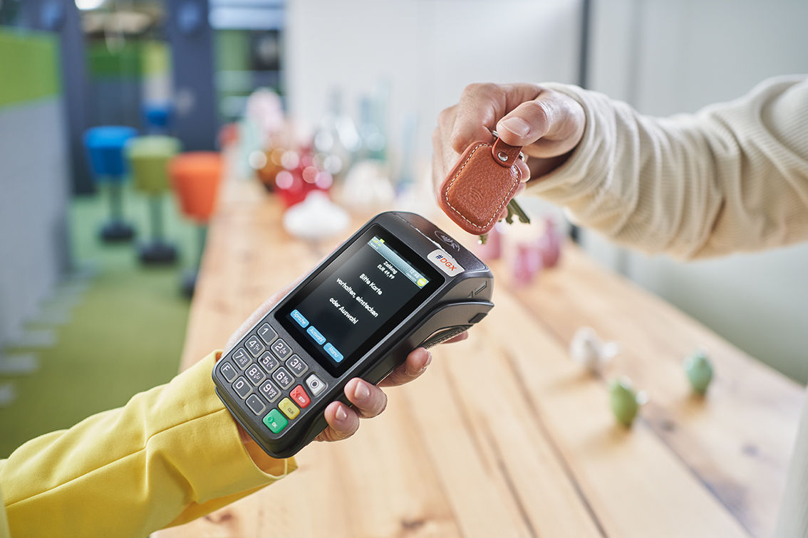 Mit einem braunen Schlüsselanhänger wird an einem NFC fähigen Kartenlesegerät bezahlt.