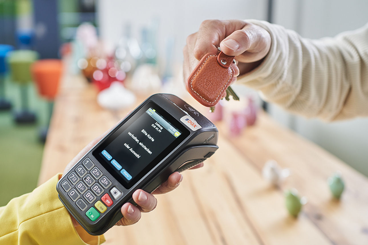 Mit einem braunen Schlüsselanhänger wird an einem NFC fähigen Kartenlesegerät bezahlt.
