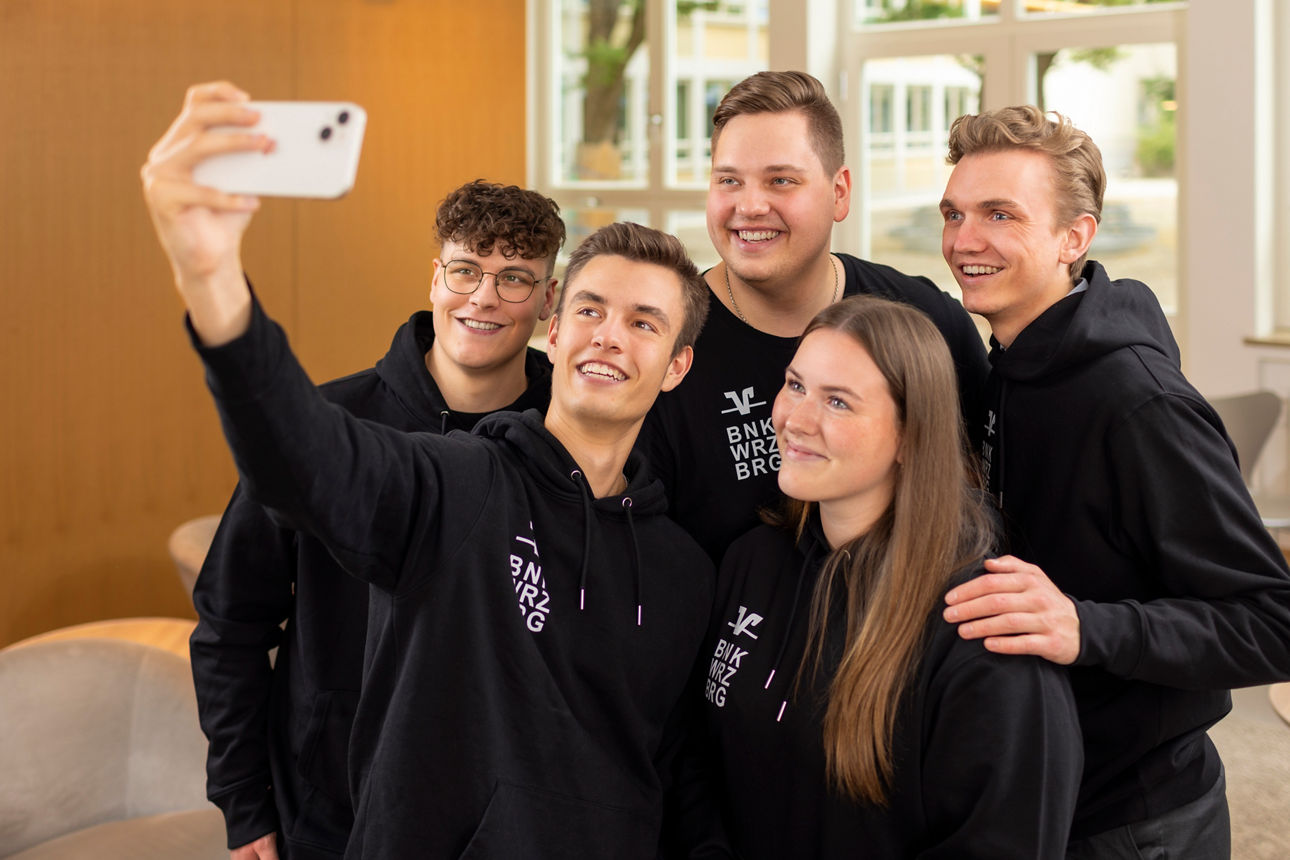 Bild von jungen Leuten in Hoodies im Design der VR-Bank Würzburg, die ein Selfie machen.